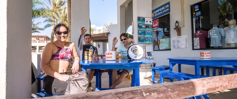 Trois personnes souriantes assises à une table devant un centre de plongée