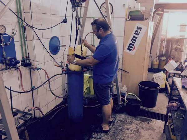 Un homme manipule une bouteille de plongée dans un atelier carrelé