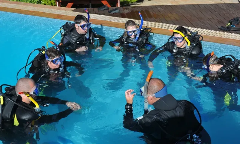Groupe de plongeurs en formation dans une piscine, instructeur expliquant