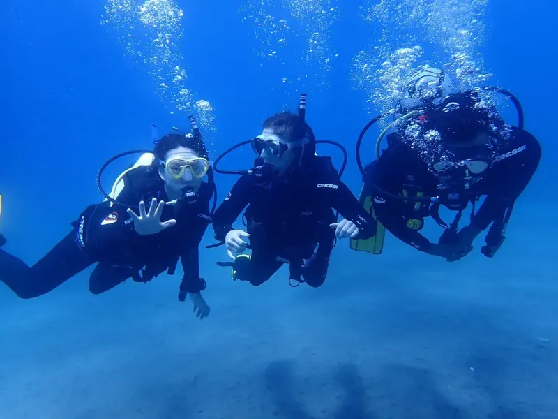 Trois plongeurs en combinaison explorent les fonds marins bleus