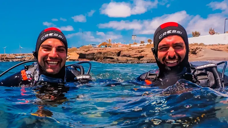 Deux plongeurs souriants émergent de l'eau, équipés et heureux