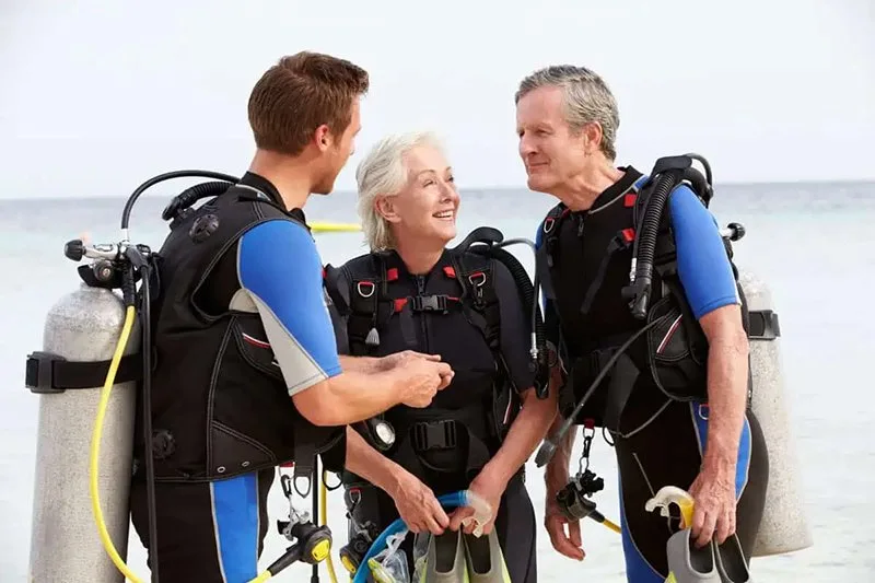 Trois plongeurs souriants équipés sur une plage ensoleillée