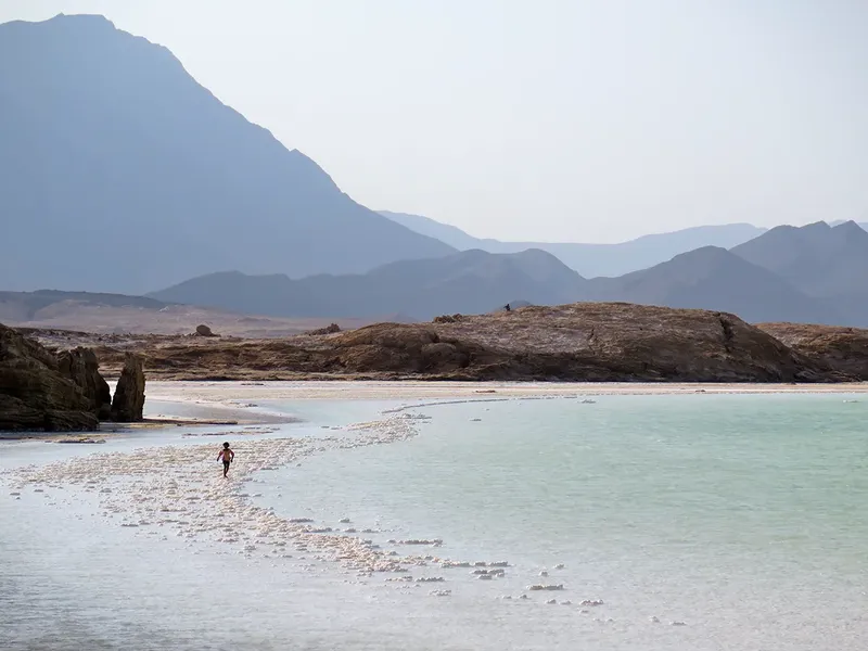 Une personne marche dans l'eau peu profonde sur une plage rocheuse
