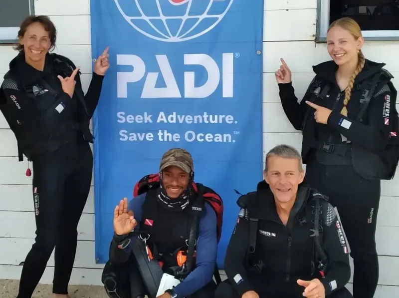 Quatre plongeurs souriants posent devant une bannière PADI bleue