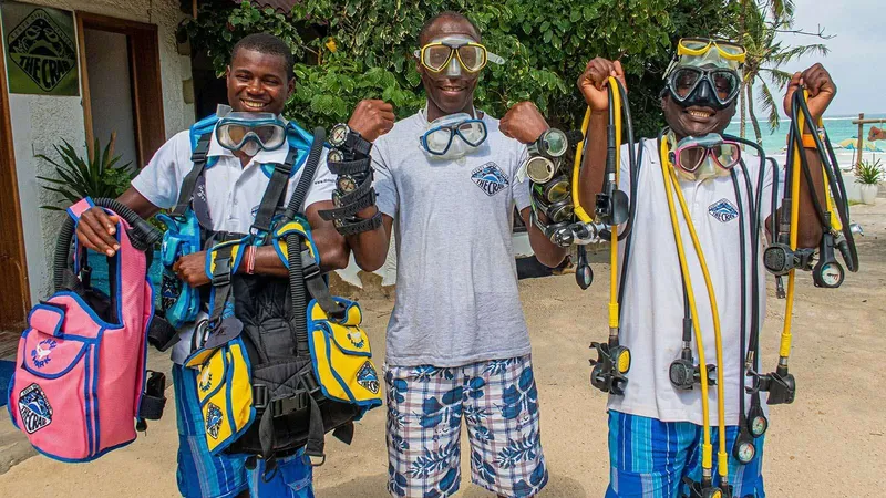 Trois plongeurs souriants équipés de matériel de plongée devant un bâtiment