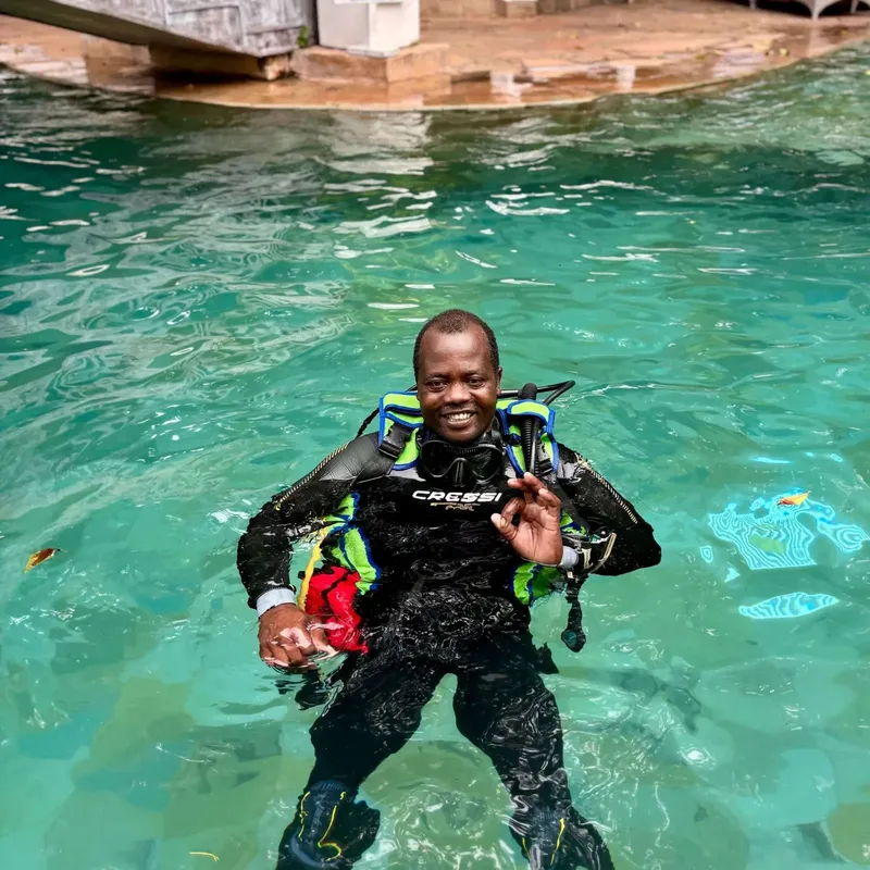 Plongeur souriant en combinaison, équipé, dans une eau turquoise claire