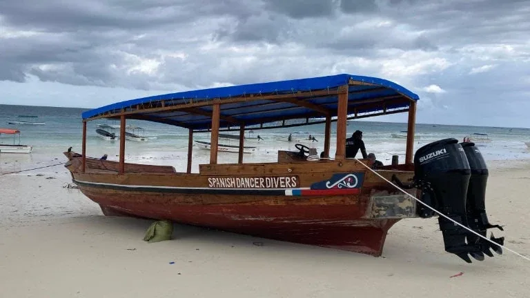 Bateau de plongée échoué sur une plage de sable blanc nuageux