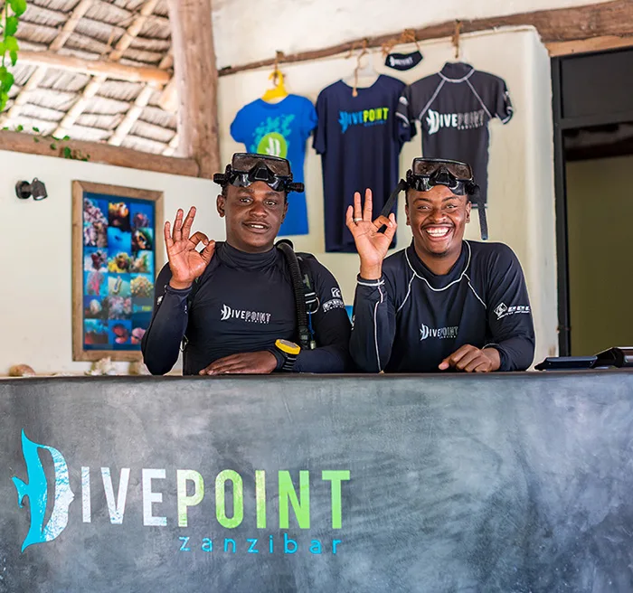 Deux plongeurs souriants avec leur équipement devant un comptoir