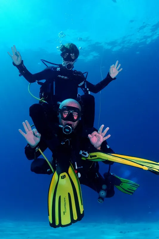 Deux plongeurs souriants avec leurs bras levés dans l'eau bleue
