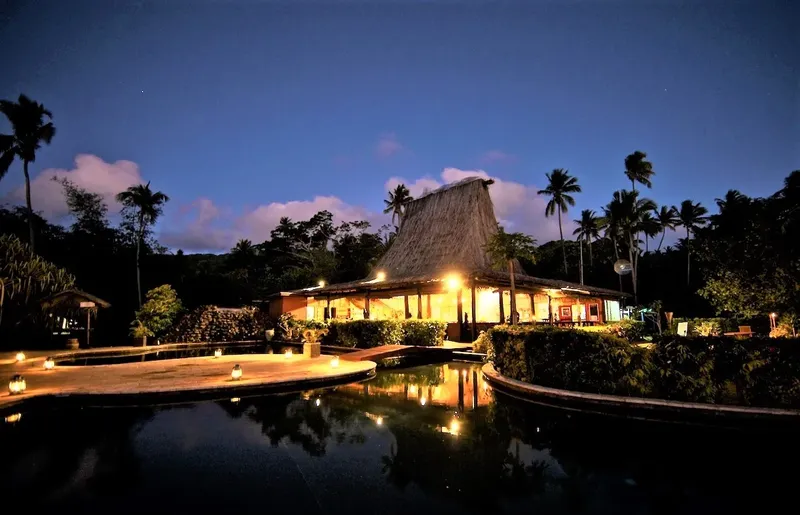Bâtiment éclairé au crépuscule avec végétation tropicale et piscine sombre