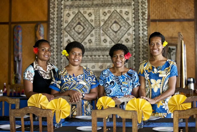 Quatre femmes souriantes, portant des fleurs dans les cheveux, assises
