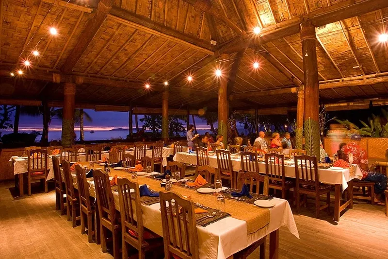 Salle à manger ouverte sur la mer avec tables dressées et convives