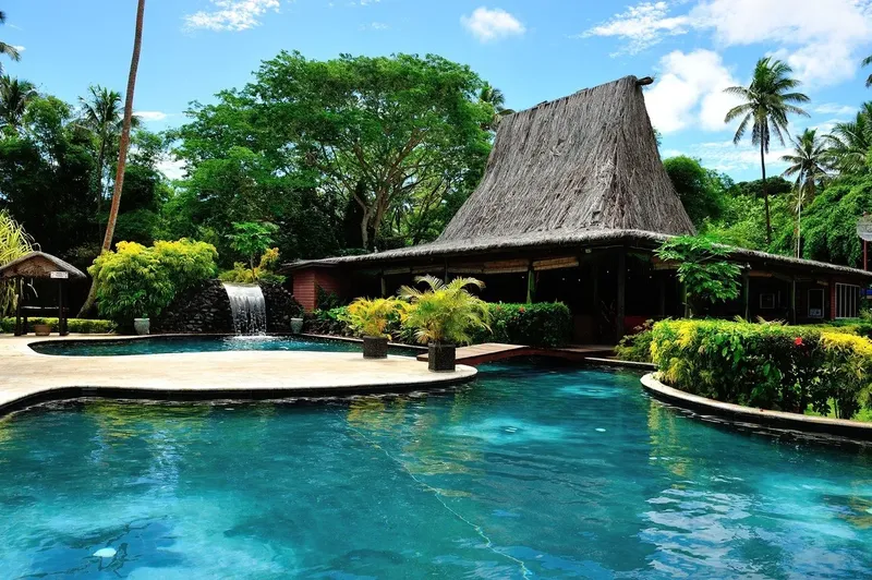 Bâtiment exotique avec toit de chaume près d'une piscine turquoise