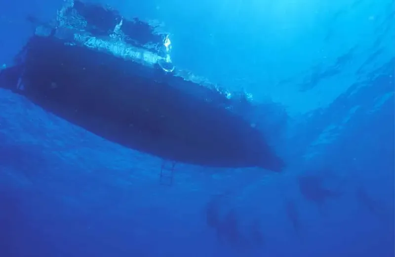 Vue sous-marine d'une coque de bateau sombre dans l'eau bleue