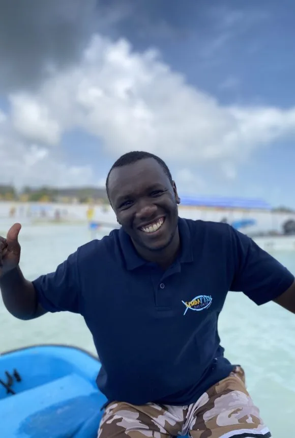 Homme souriant, portant un polo bleu avec un logo, en extérieur