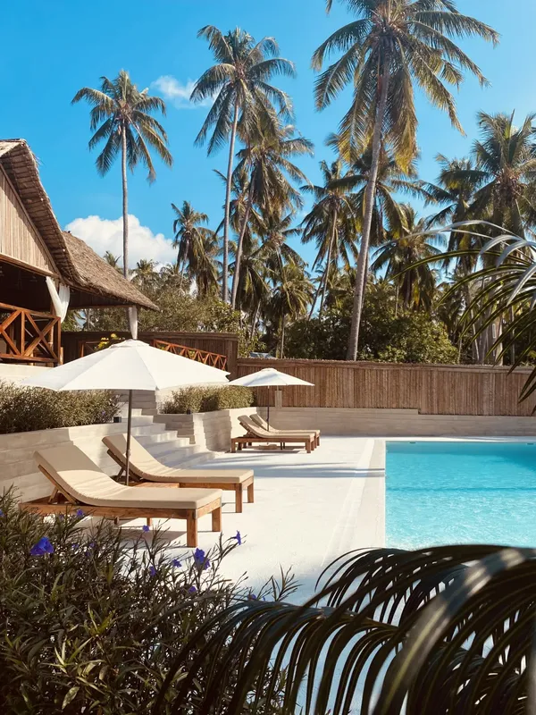 Piscine bordée de transats et de palmiers sous un ciel bleu