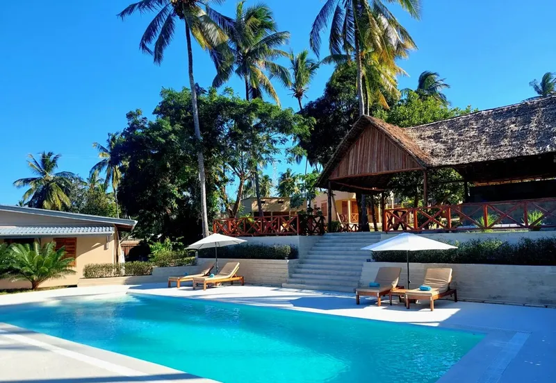 Piscine turquoise devant bâtiments et végétation luxuriante sous ciel bleu