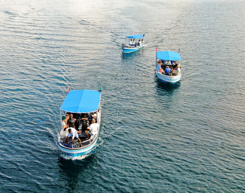 Trois bateaux de plongée bleus naviguent sur une mer calme et ensoleillée