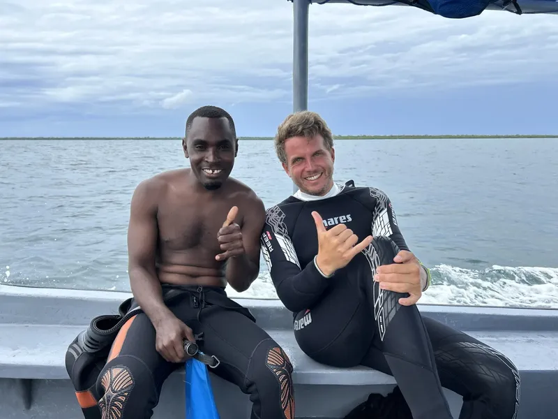 Deux plongeurs souriants font un signe de la main sur un bateau