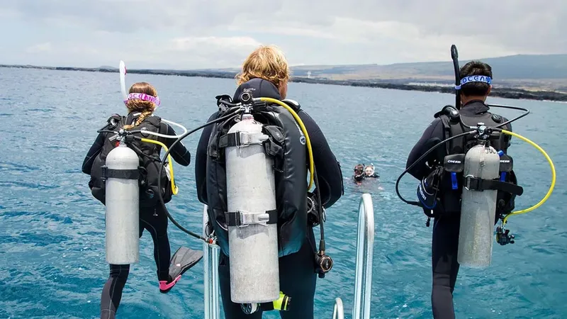 Trois plongeurs équipés se préparent à entrer dans l'eau depuis un bateau