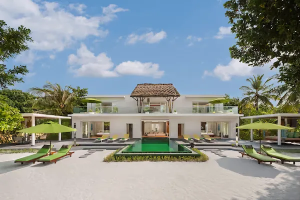 Bâtiment blanc moderne avec piscine, transats et végétation tropicale