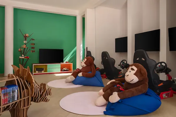 Salle de jeux avec des fauteuils poire, des consoles et des singes en peluche