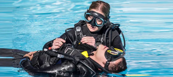 Deux plongeurs en combinaison, un aide l'autre dans l'eau