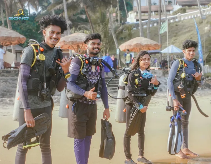 Quatre plongeurs équipés sourient à la caméra sur une plage