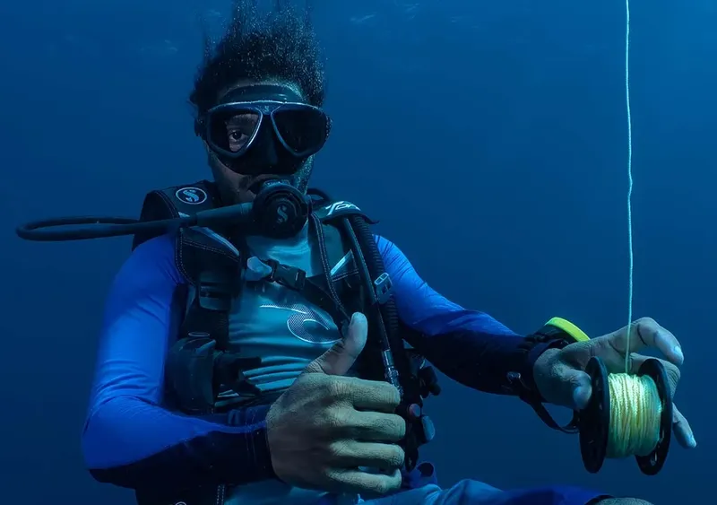 Plongeur manipulant une bobine de fil dans l'eau bleue