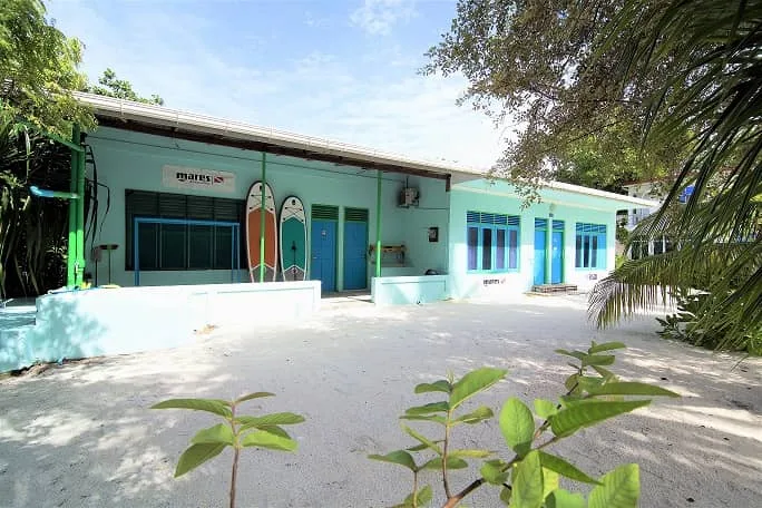 Façade d'un bâtiment turquoise avec deux planches de surf adossées