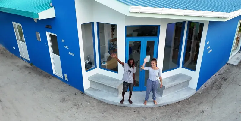 Deux personnes souriantes devant la façade bleue d'un bâtiment