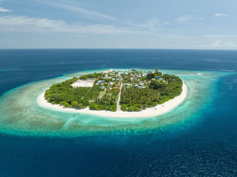 Île tropicale avec végétation dense, plage de sable blanc et bâtiments