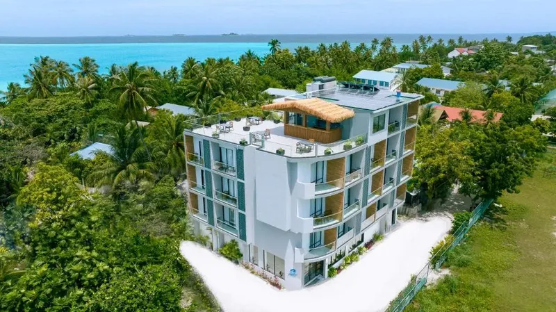 Bâtiment moderne blanc avec terrasses, végétation luxuriante et mer turquoise