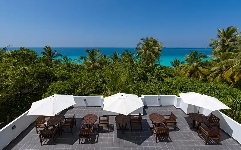 Terrasse avec tables, chaises et parasols vue sur mer et végétation
