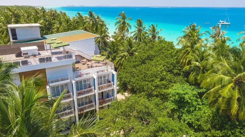 Vue aérienne d'un bâtiment blanc avec des palmiers et une plage turquoise