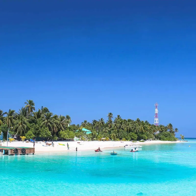 Plage tropicale avec bateaux, personnes et eau turquoise sous ciel bleu