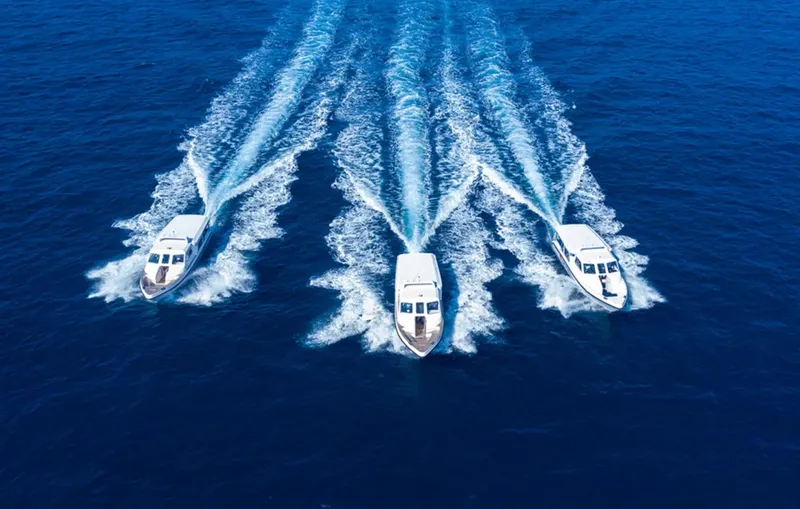 Trois bateaux de plongée rapides naviguent sur une mer bleue claire