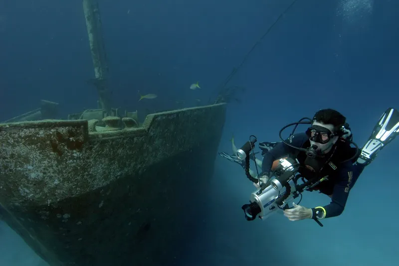 Plongeur avec appareil photo explore une épave sous-marine bleu profond