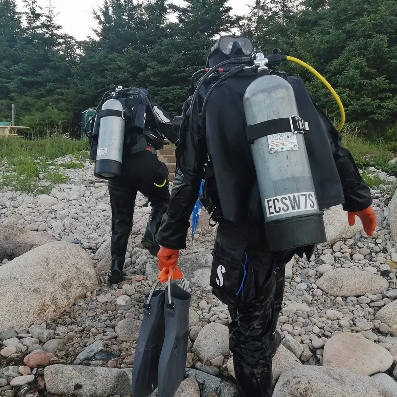 Deux plongeurs équipés marchent sur un chemin de galets