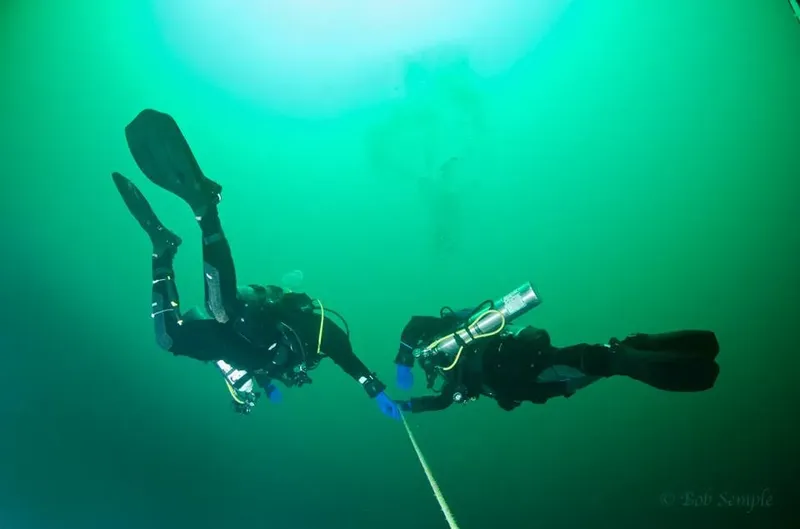 Deux plongeurs en combinaison explorent les profondeurs sous-marines, nageant face à face