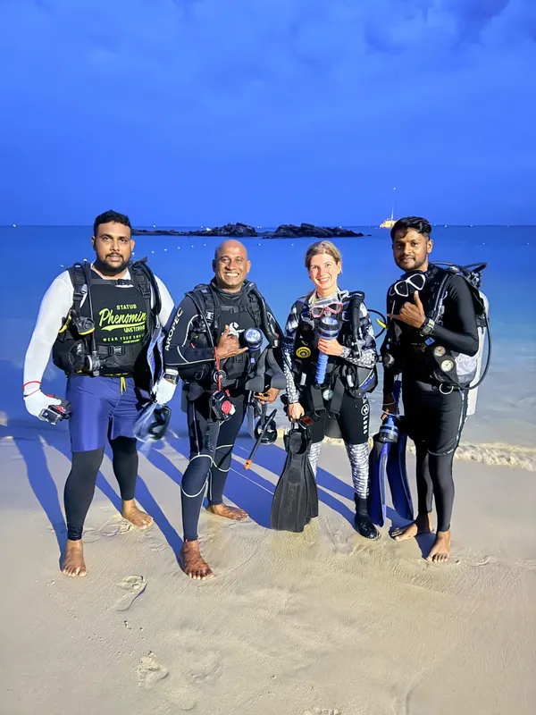 Quatre plongeurs souriants posent sur une plage de sable blanc