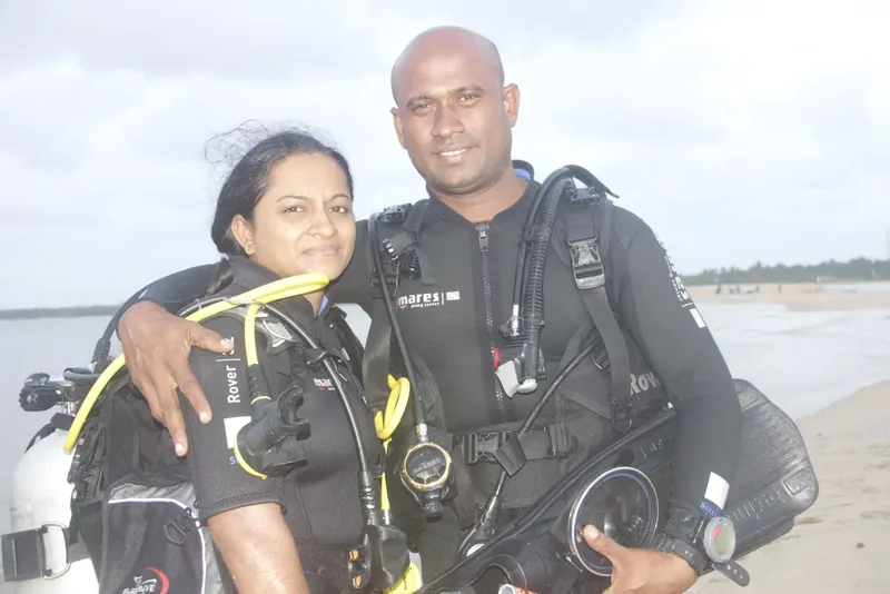 Couple de plongeurs souriants, équipés, devant une plage ensoleillée