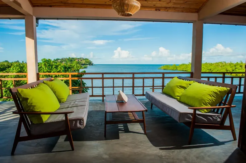 Terrasse ombragée avec canapés verts donnant sur la mer bleue