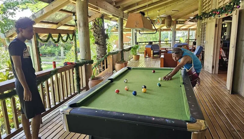 Deux personnes jouent au billard sur une terrasse en bois ombragée