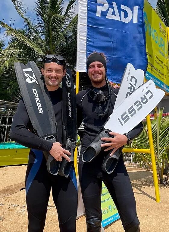 Deux plongeurs souriants avec palmes et masque devant une bannière PADI