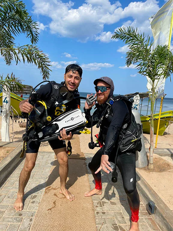 Deux plongeurs souriants équipés sur une plage ensoleillée