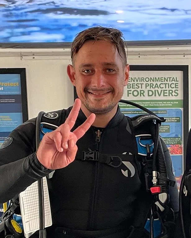 Plongeur souriant en combinaison, faisant un signe de la main