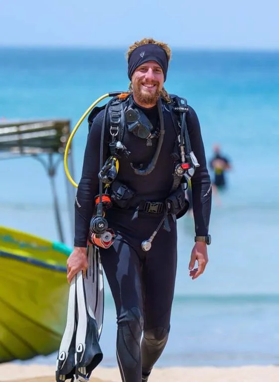 Plongeur souriant en combinaison complète marchant sur une plage ensoleillée