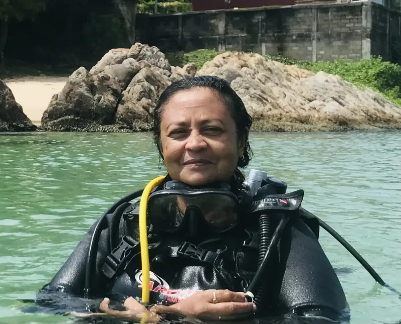 Plongeuse souriante en combinaison, masque et détendeur dans l'eau