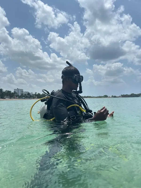 Plongeur en combinaison équipé, partiellement immergé dans une eau turquoise